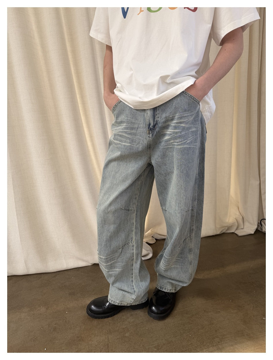 Close view of loose light-wash jeans with whiskering and articulated seams, worn with a white graphic T-shirt.