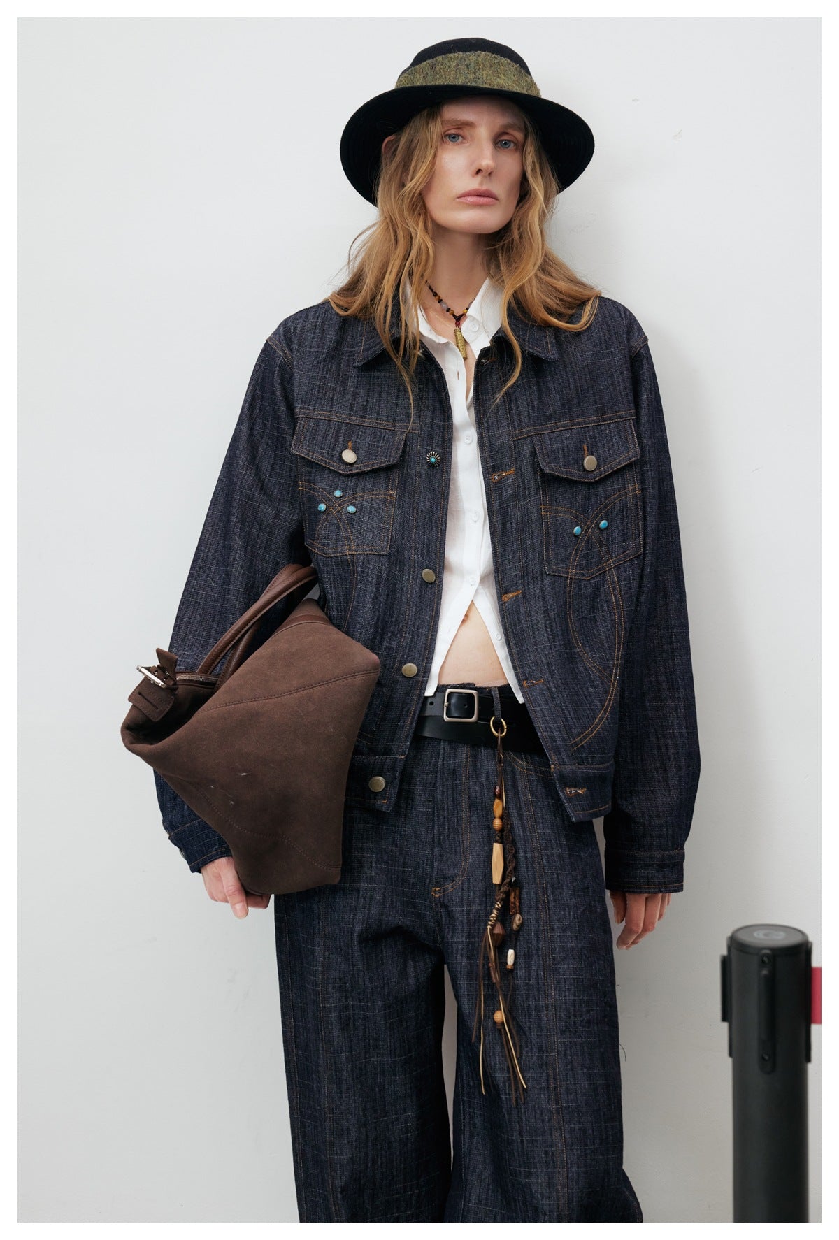 Model wearing a dark indigo denim jacket with turquoise accents and matching wide-leg trousers, styled with a white shirt and