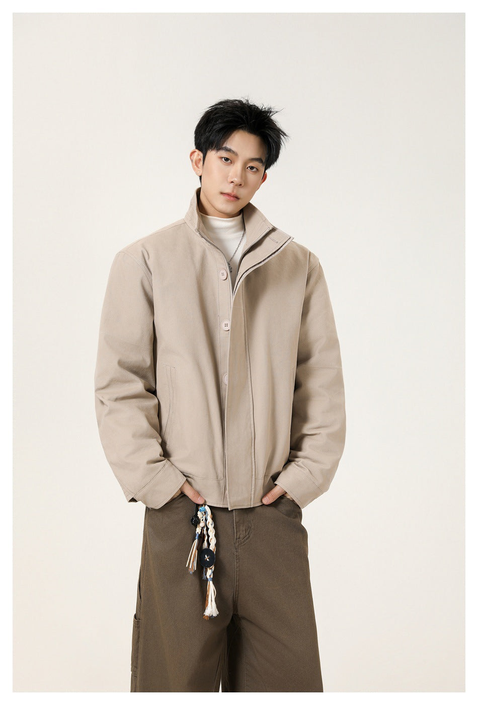 Model wearing a beige jacket with a raised collar, button front, and visible zipper over a white top.