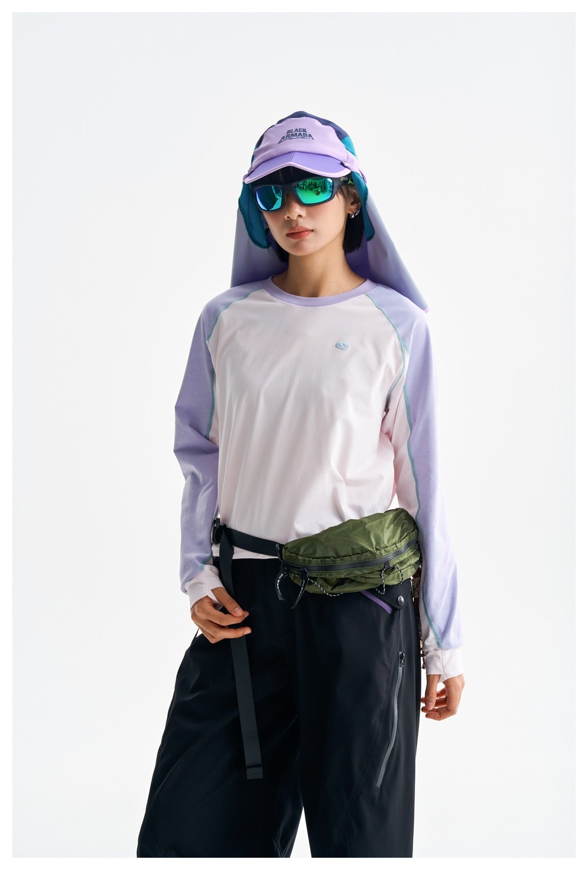 Woman wearing a white raglan long-sleeve top with lavender sleeves and teal seams, paired with black trousers.
