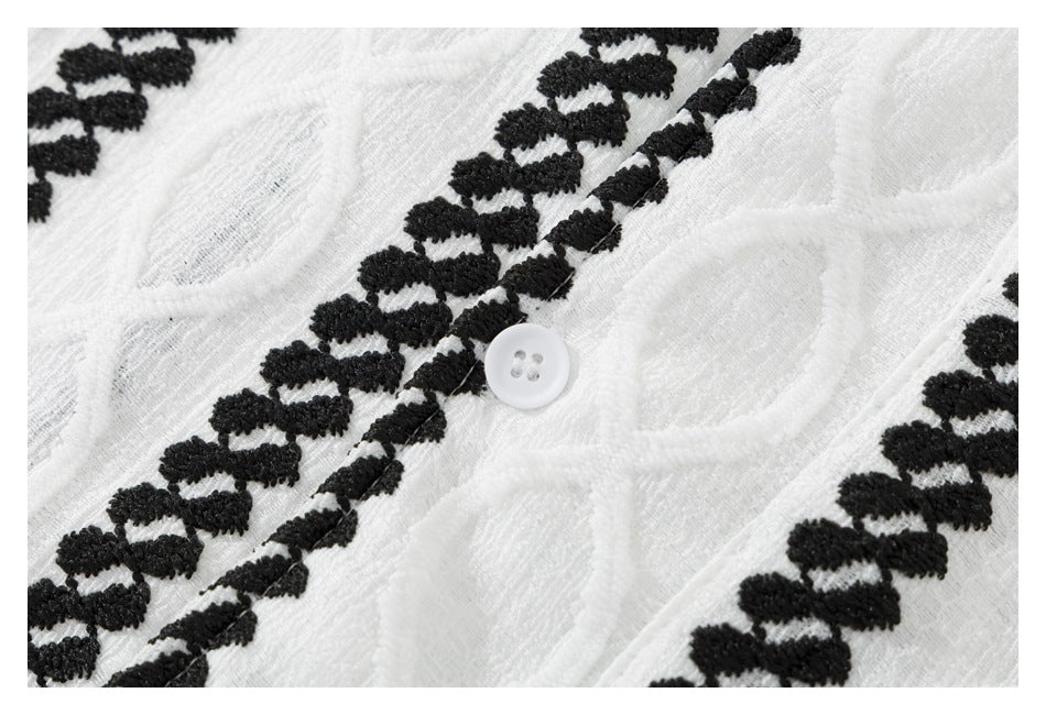 Close-up of a white button on textured white fabric with raised black embroidered bands.