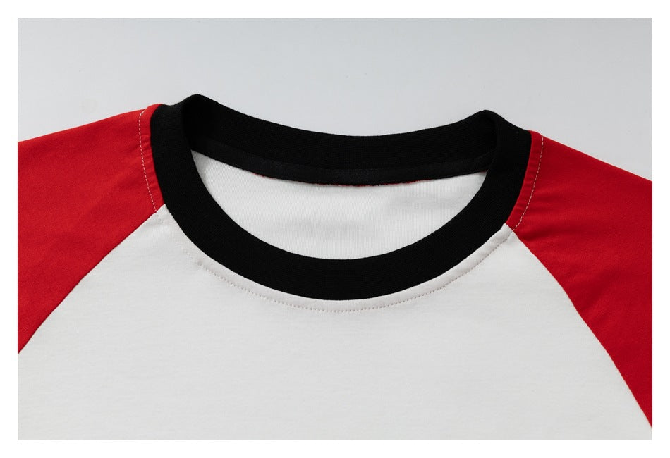 Close-up of a white raglan shirt with red shoulder panels and a black ribbed crew neck.