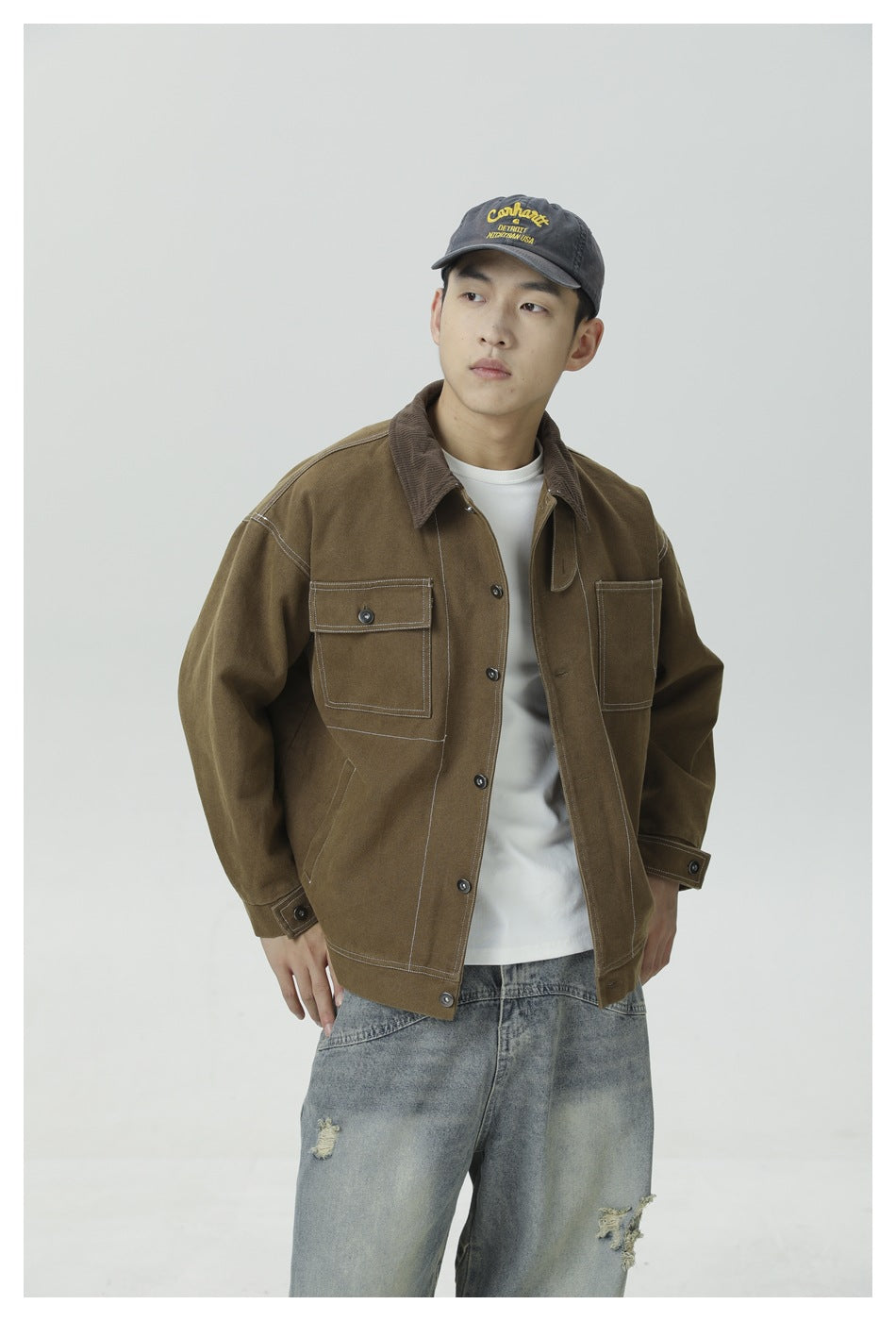 Closer view of a model in a brown work jacket with contrast stitching, corduroy collar, and buttoned chest pocket.