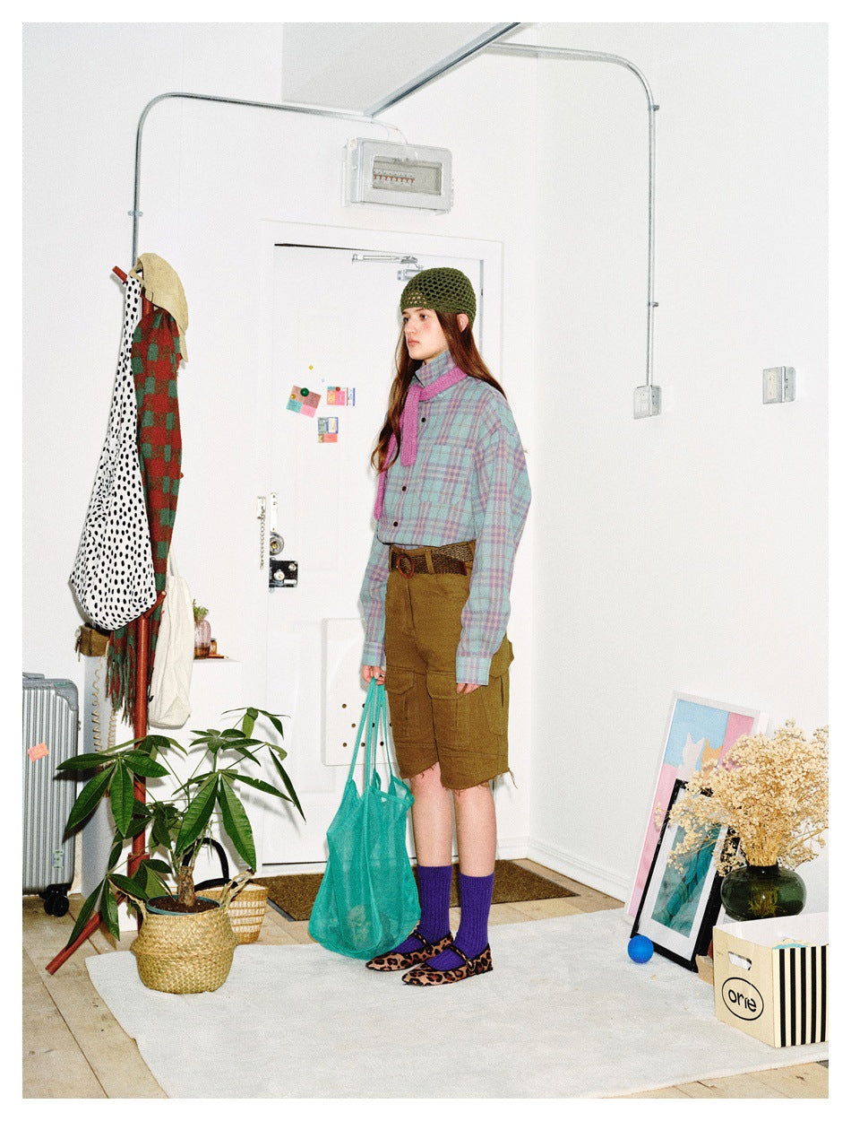 Side view of a model in a pastel plaid button-up shirt, olive cargo shorts, purple socks and a green knit cap.