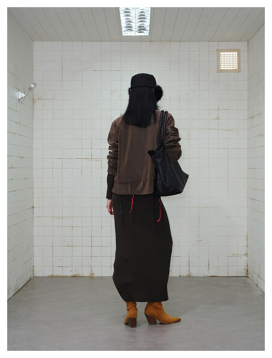 Back view of a model wearing a dark brown jacket and long black skirt, with a black shoulder bag.