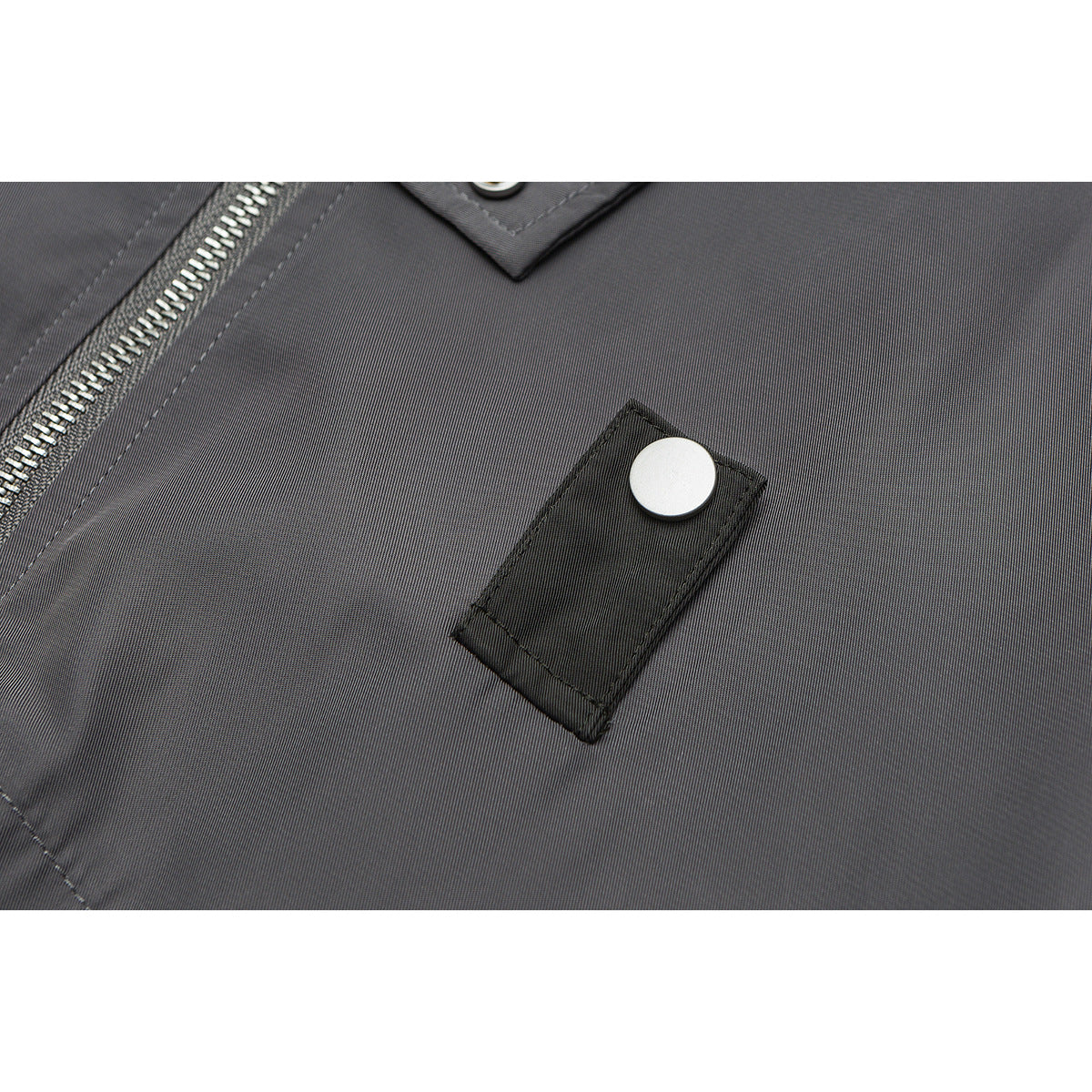 Close-up of a gray jacket chest with a black snap tab and part of the silver zipper.