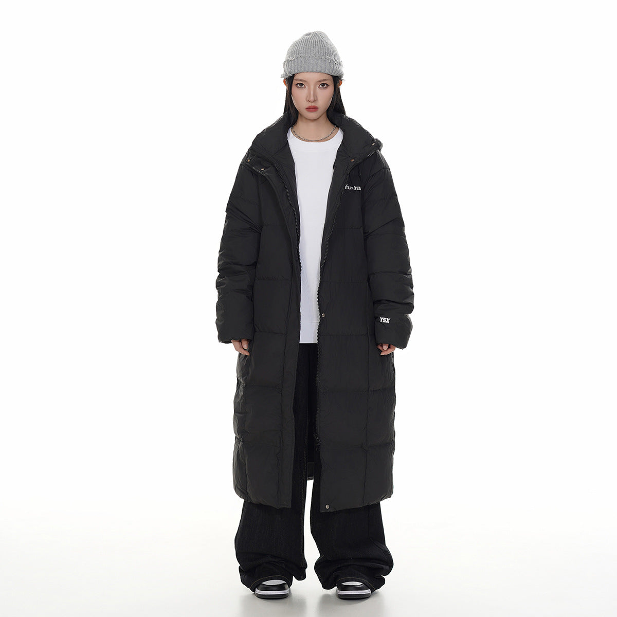 Front view of a model wearing an open long black hooded puffer coat over a white top.