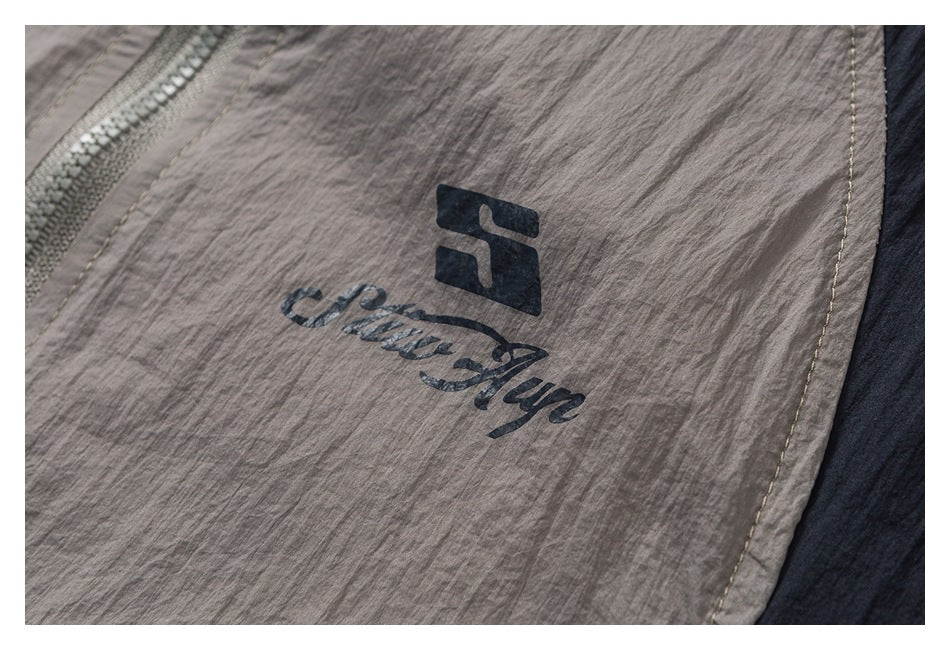 Printed dark logo on a taupe-gray garment panel beside a dark contrast section.