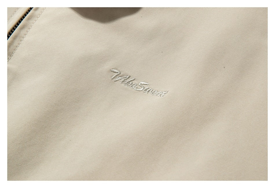 Close-up of small embroidered script on beige fabric beside a zipper edge.