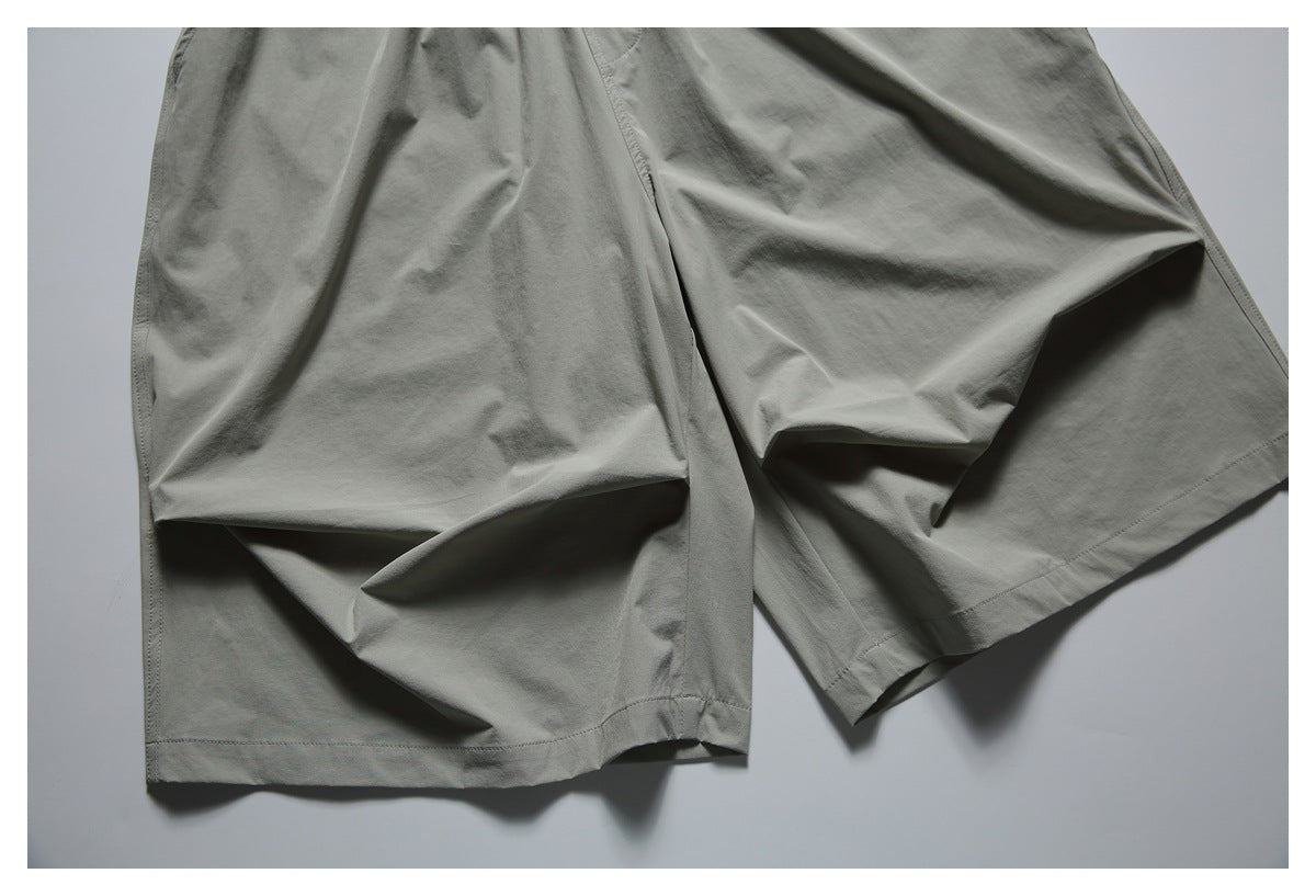 Close-up of the gray-green shorts' loose legs and stitched hems, laid flat.
