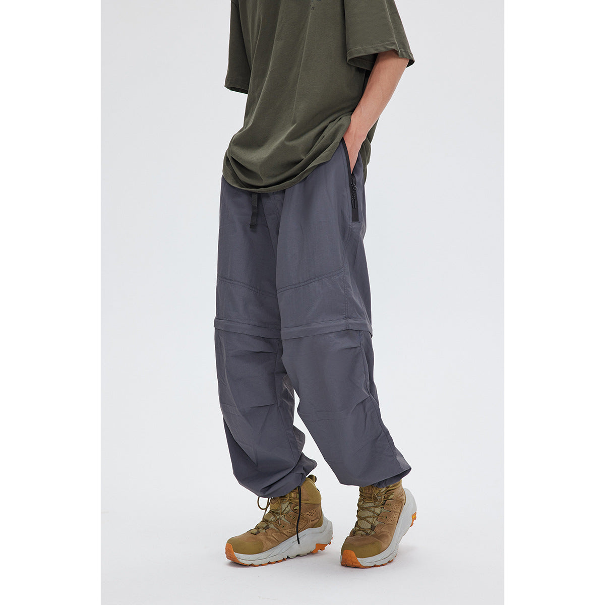 Angled view of a model wearing loose slate-gray convertible pants with zip pockets and hiking shoes.