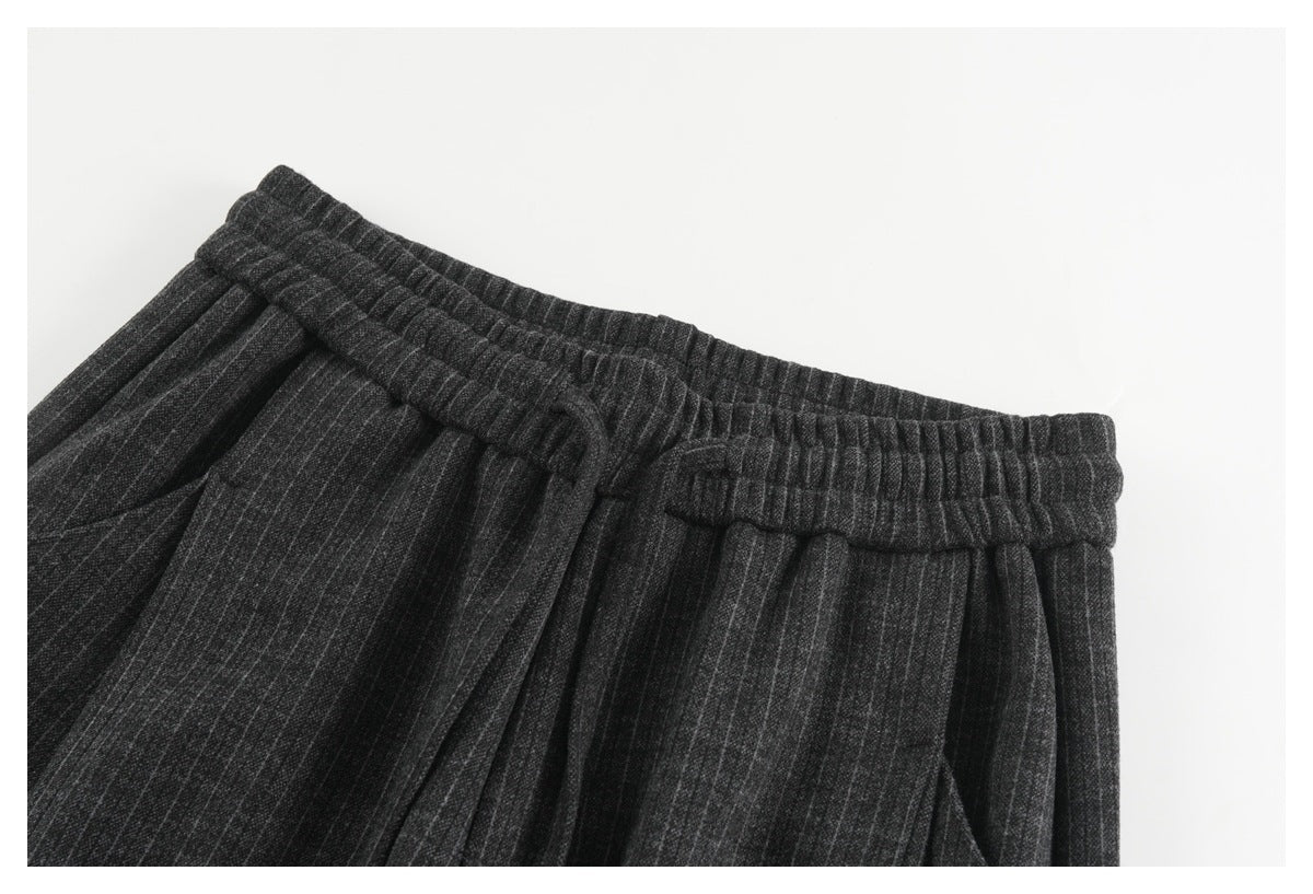 Close-up of charcoal pinstripe trousers showing the elastic waistband, drawstring, and front pleats.