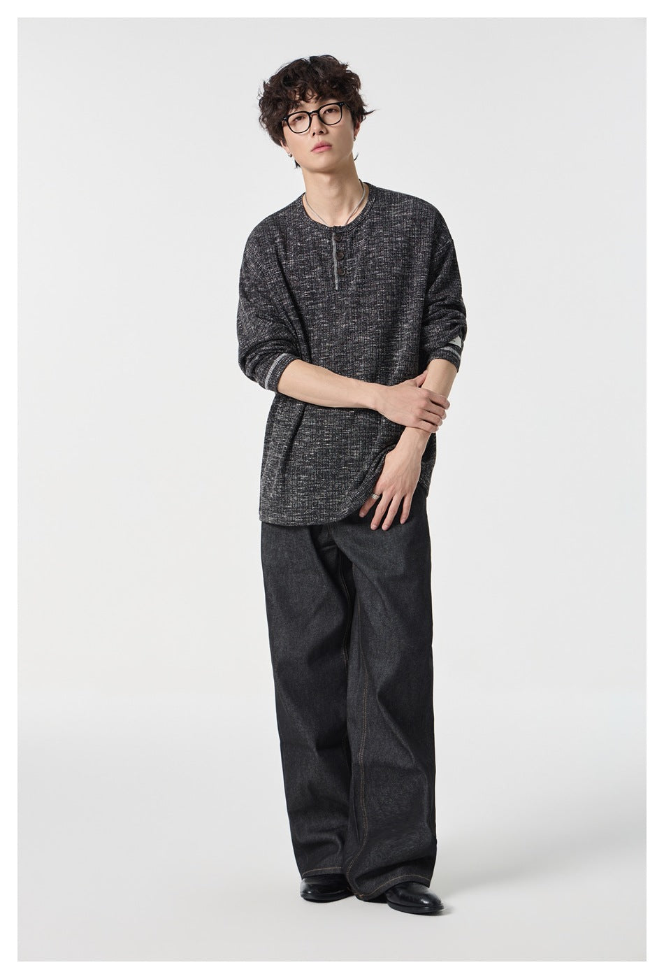 Full-length view of a man in a black heathered knit henley top with wide-leg dark jeans and black shoes