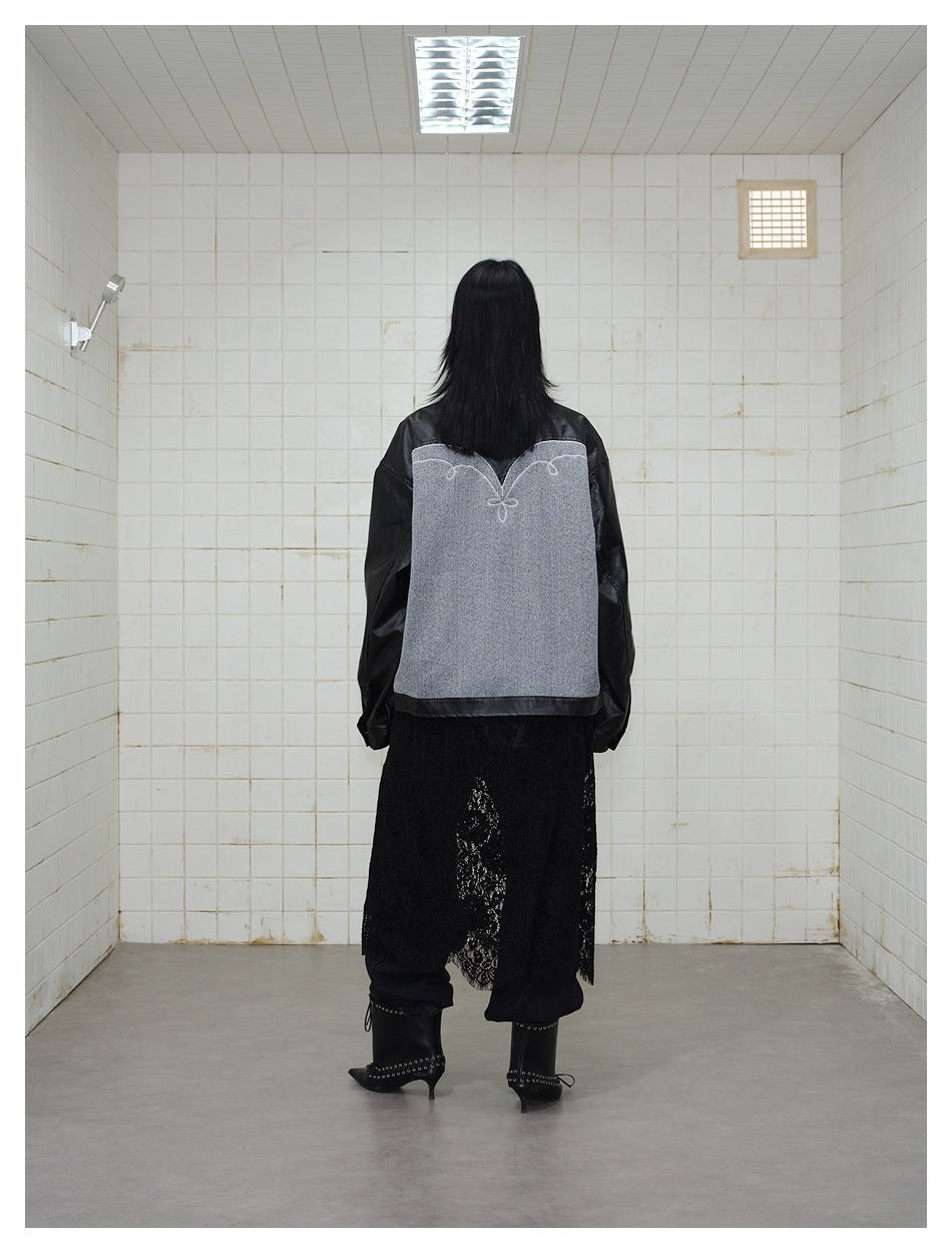 Back view of a model wearing a black jacket with a large gray panel and white curved stitching.