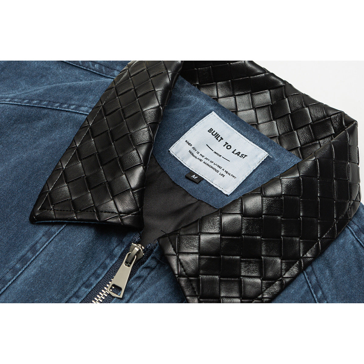Close-up of a blue denim jacket with a black woven-texture collar, zipper, and sewn-in white label.