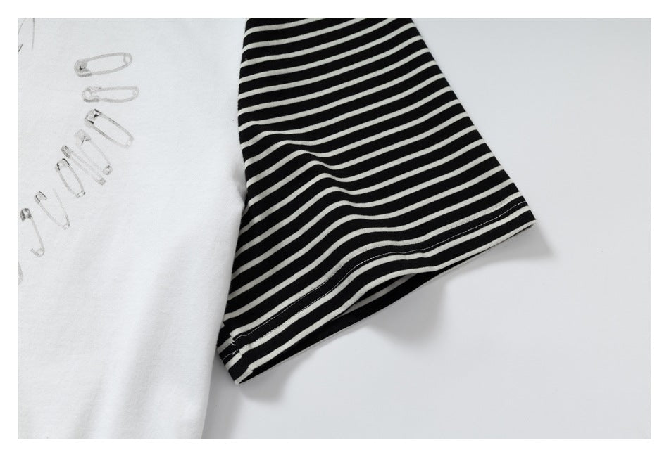 Close-up of a white shirt with a black-and-white striped sleeve and small safety-pin illustrations.