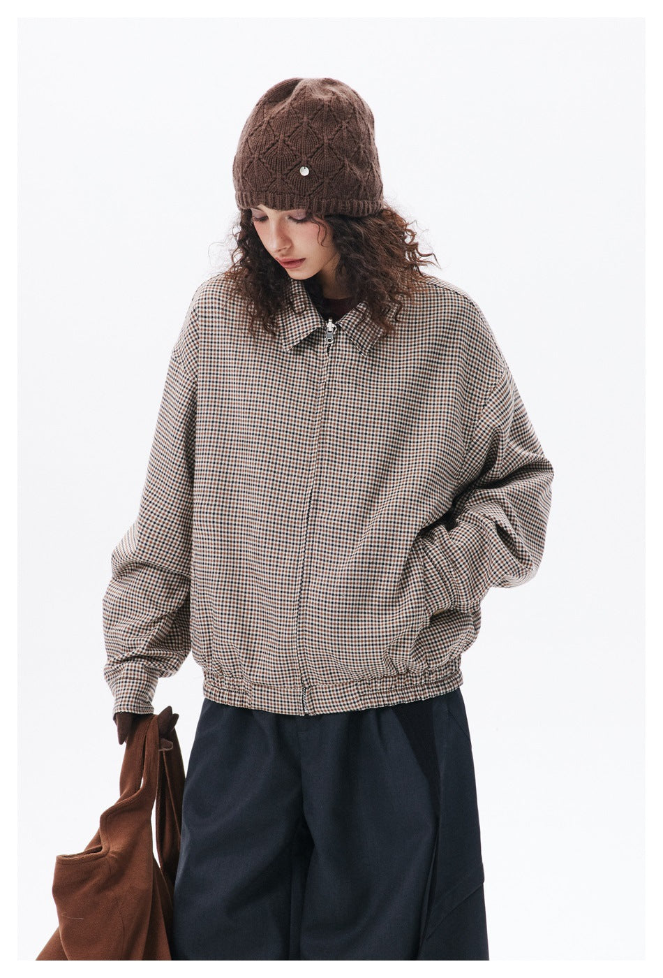 Model wearing a beige-and-brown check zip jacket with a pointed collar and navy trousers, shown with a brown knit beanie.
