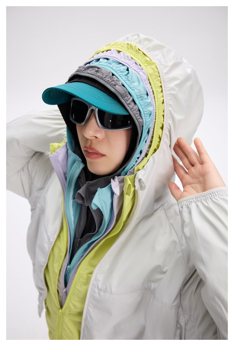 Close-up of a model wearing a white hooded jacket layered with lime, aqua, lavender, and charcoal panels, plus a teal-brim