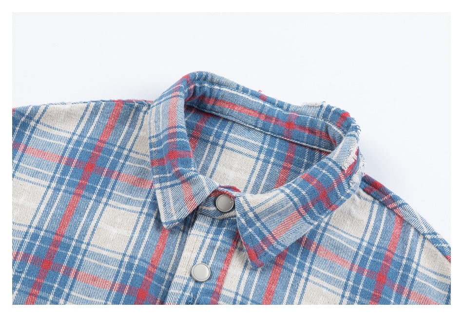 Close-up of the pointed collar and metal snap buttons on a blue, red, and cream plaid shirt.