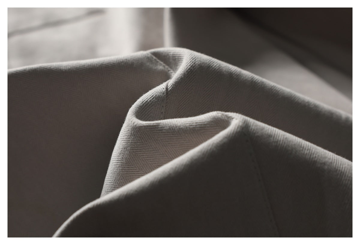 Macro view of folded gray-beige fabric showing its subtle herringbone weave and stitching.