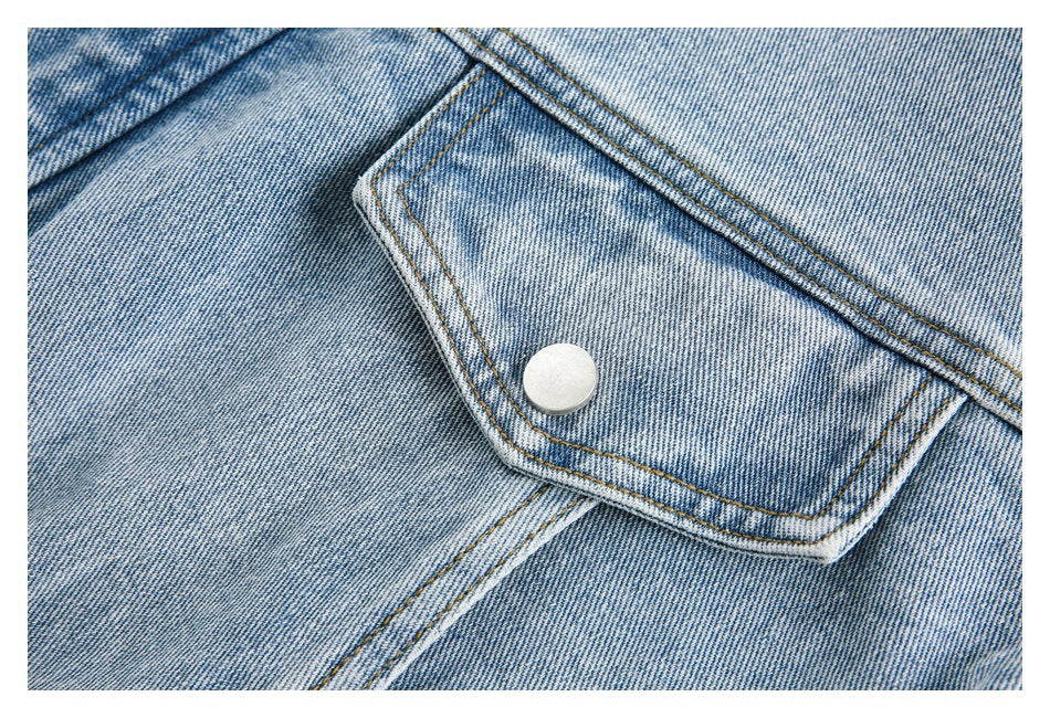 Close-up of a flap pocket with a silver snap and contrast stitching on faded blue denim.