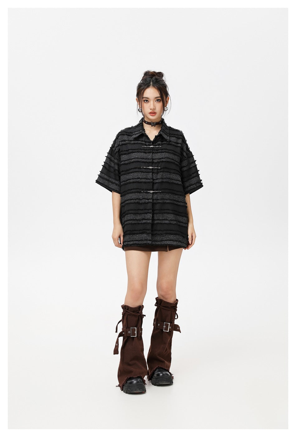 Front view of a model wearing an oversized black striped shirt with metal clasps, a brown mini skirt, and tall brown boots.