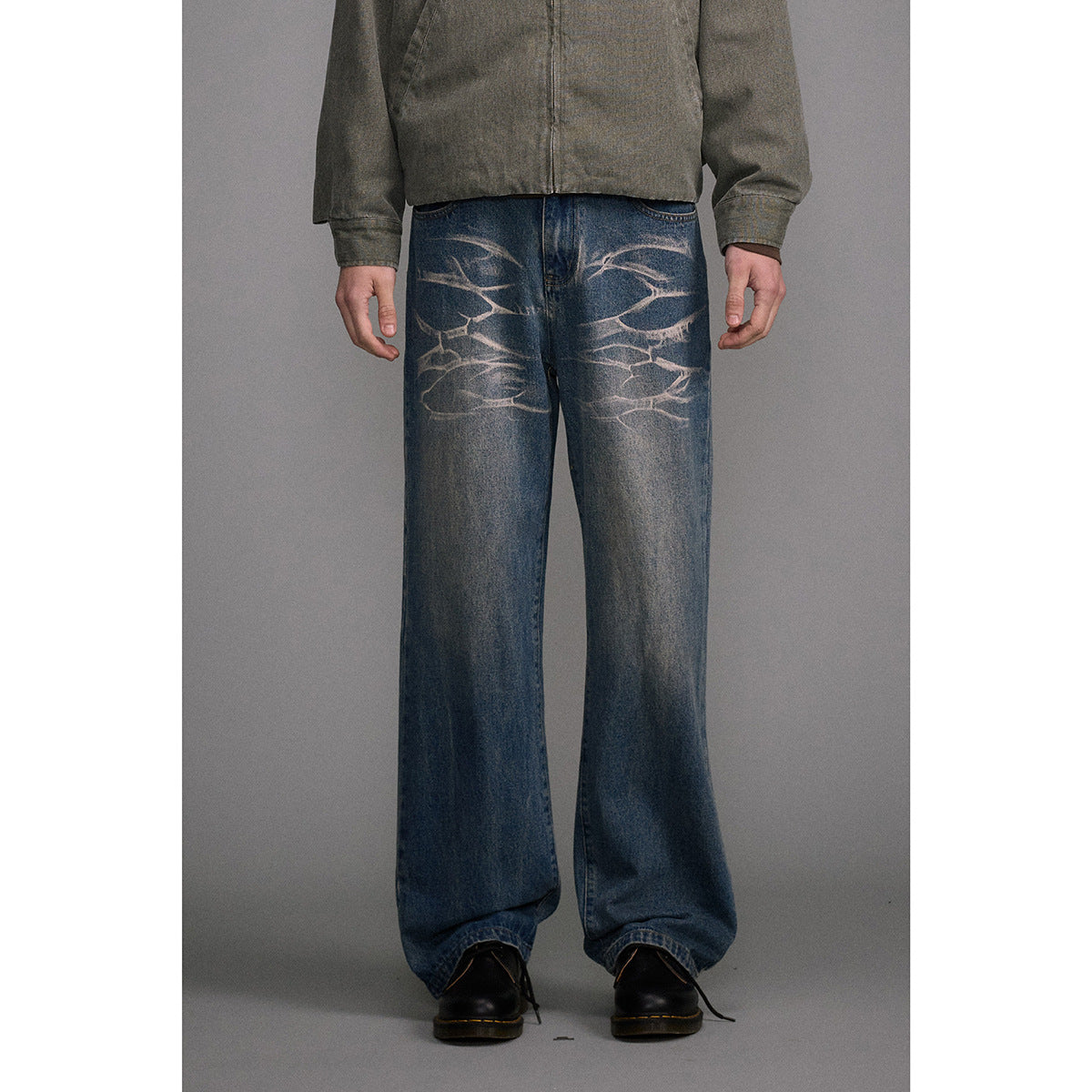 Cropped front view of a model wearing loose blue jeans with pale abstract fading across the thighs.