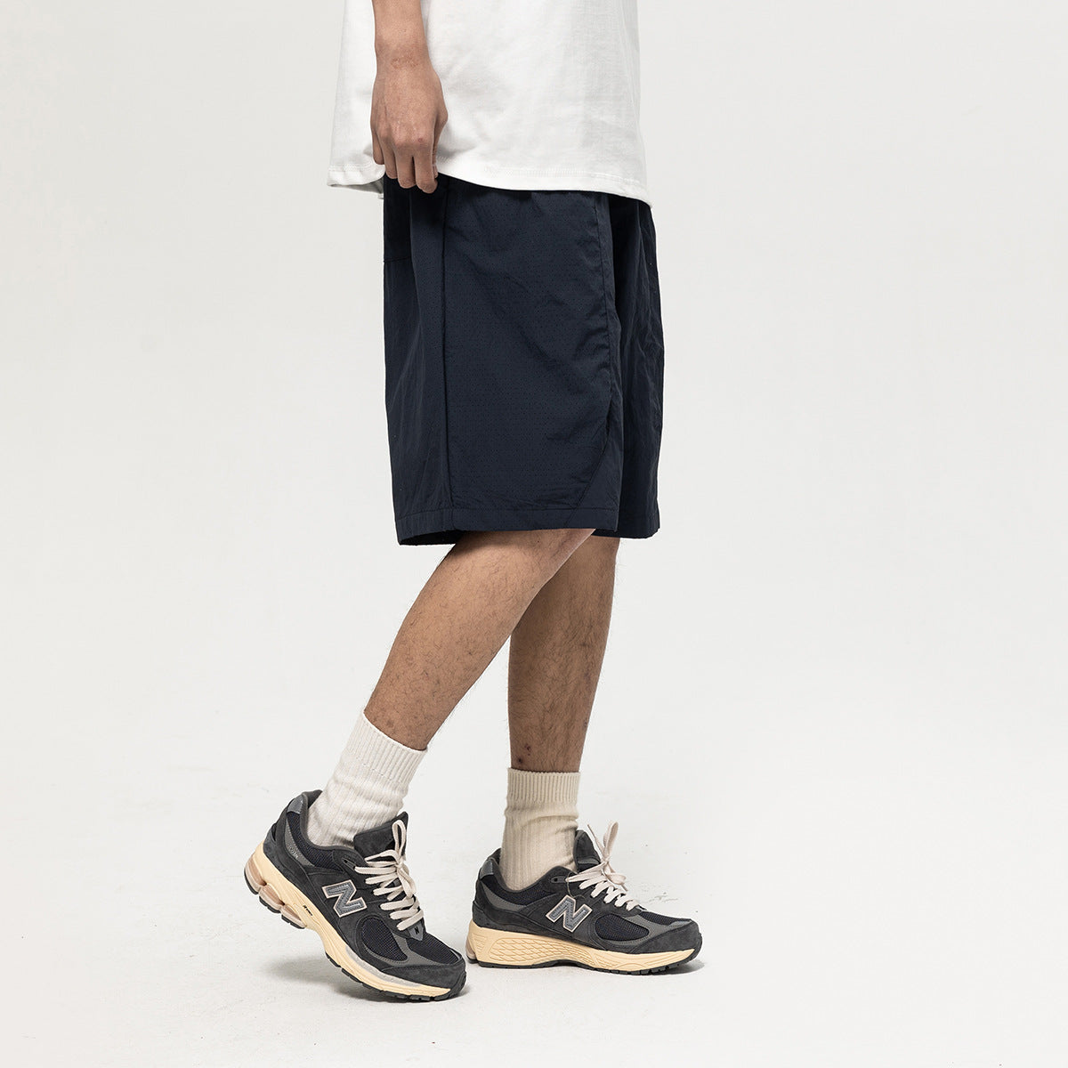 Cropped model wearing dark navy knee-length shorts with a white T-shirt and sneakers, shown from the side.