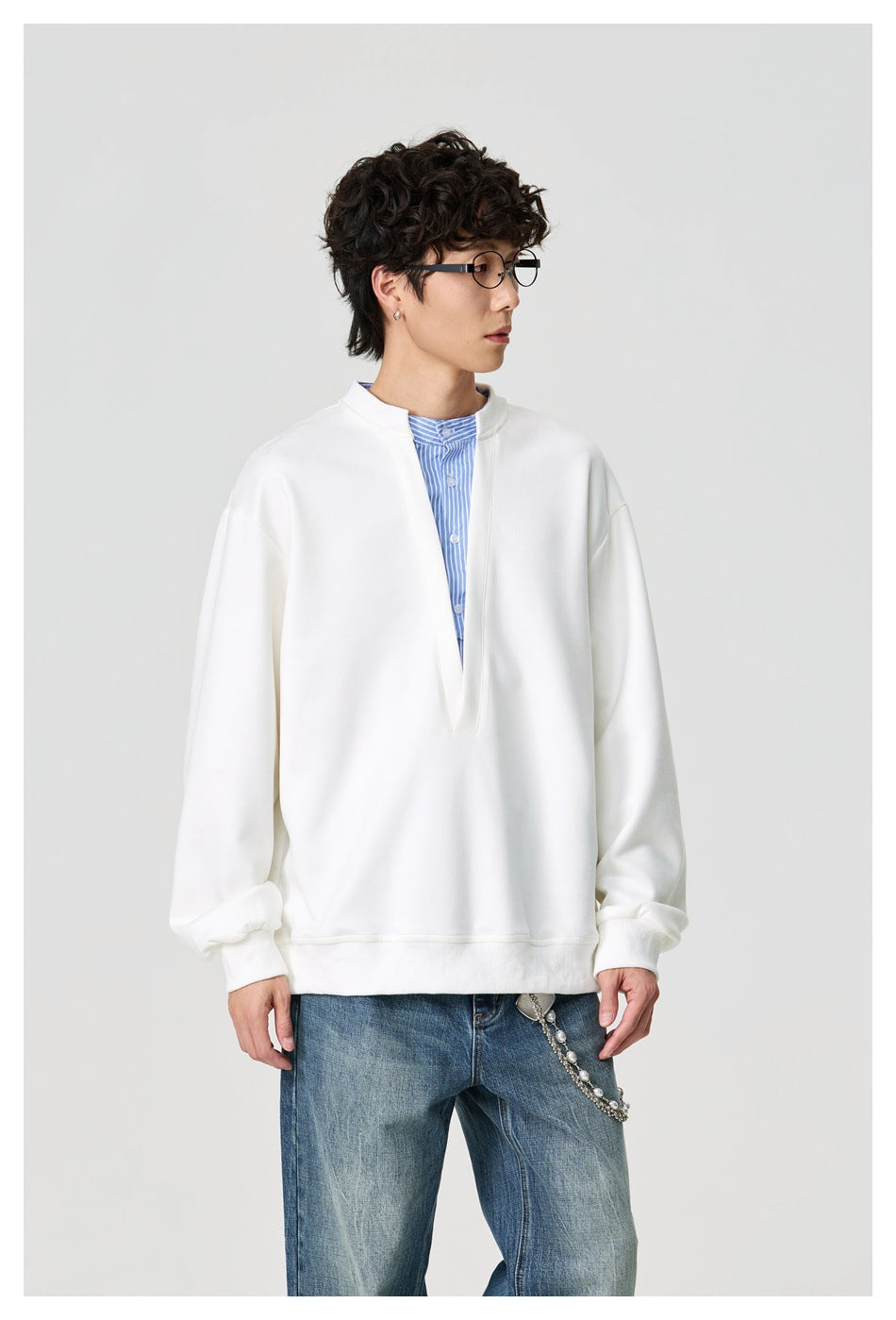 Model wearing a white oversized split-neck pullover over a blue striped shirt, shown from the front.