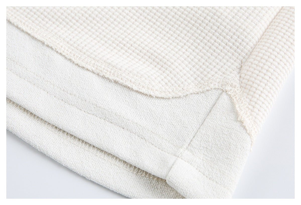Close-up of an off-white waffle-knit garment hem with folded fabric and visible stitching.