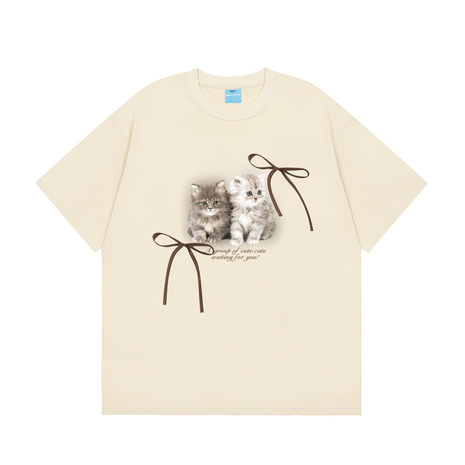 Cream short-sleeve crew-neck T-shirt with a kitten graphic, two brown ribbon bows and script text on the front