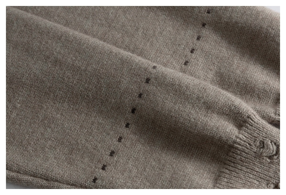 Close-up of a taupe knit sleeve with a line of small dark embroidered marks and a ribbed cuff.