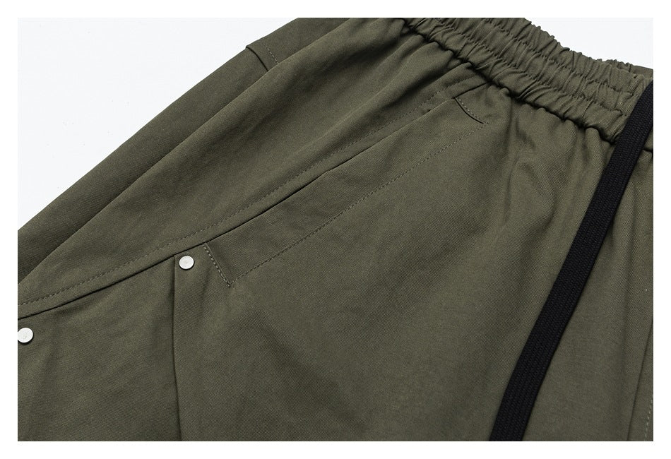 Close-up of olive trousers showing a stitched pocket, silver-tone rivets, and a black drawstring.