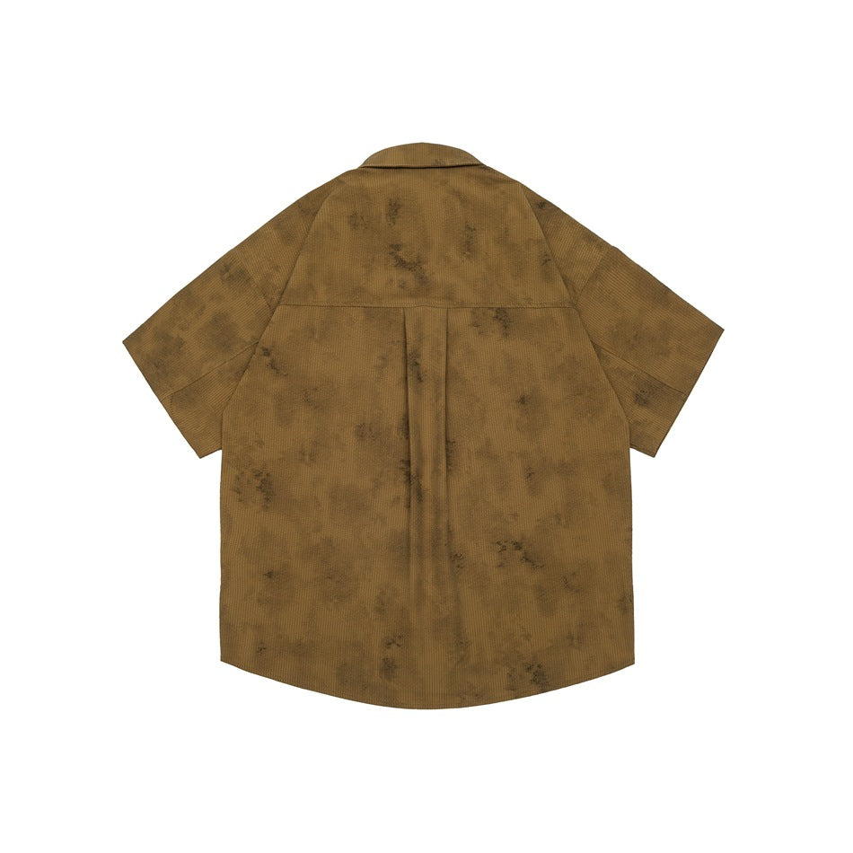 Back view of khaki-brown short-sleeve shirt with yoke seam, center box pleat and mottled distressed pattern