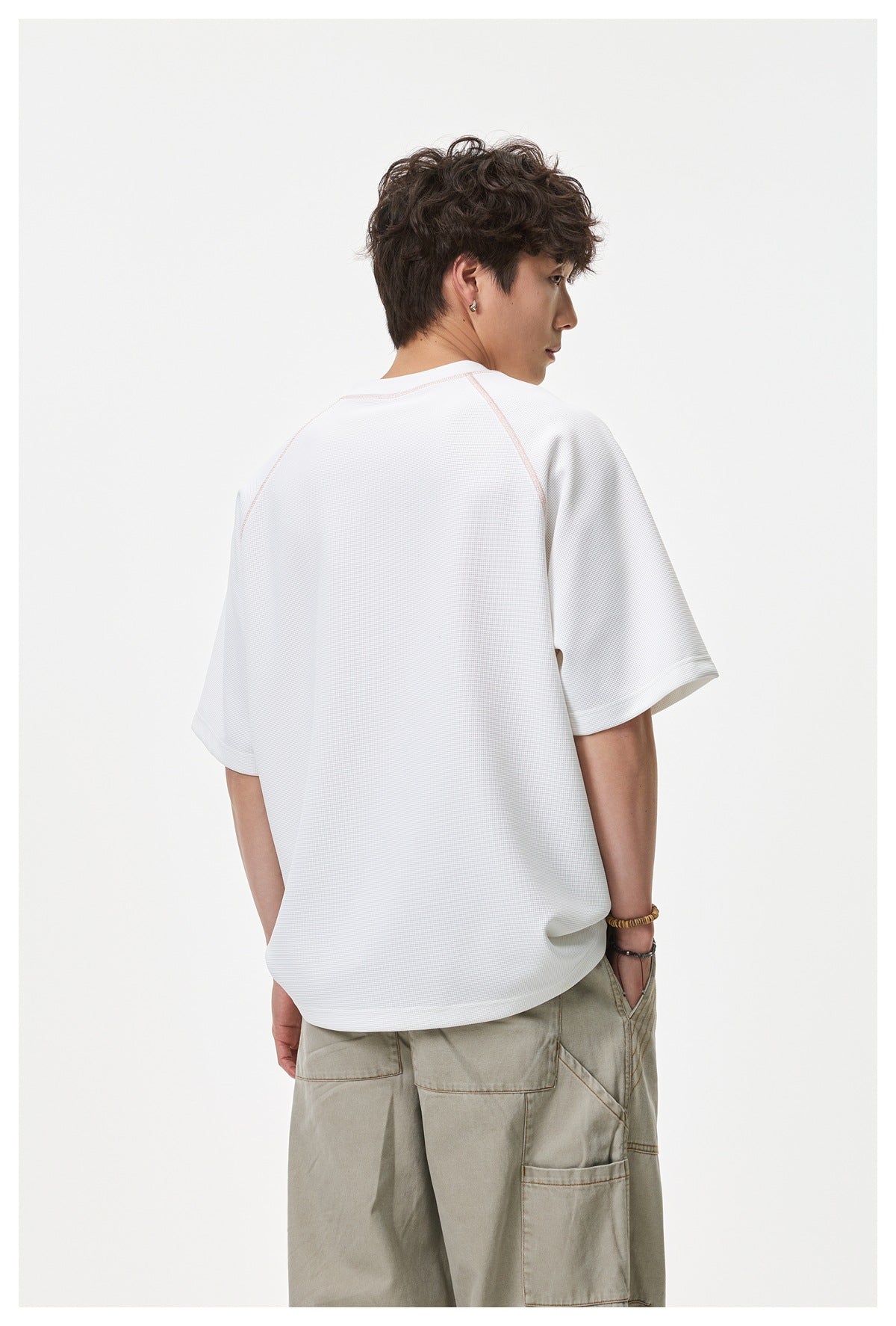 Model turned to show the back of a white textured raglan T-shirt with pale pink seam piping.