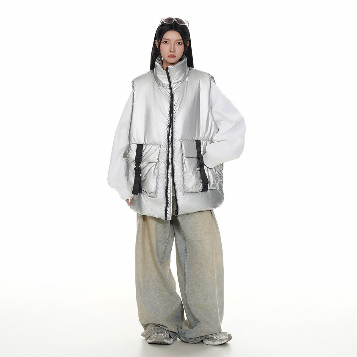 Model wearing a shiny silver padded vest with a high collar, front zip, and large buckle-detail pockets over white sleeves.