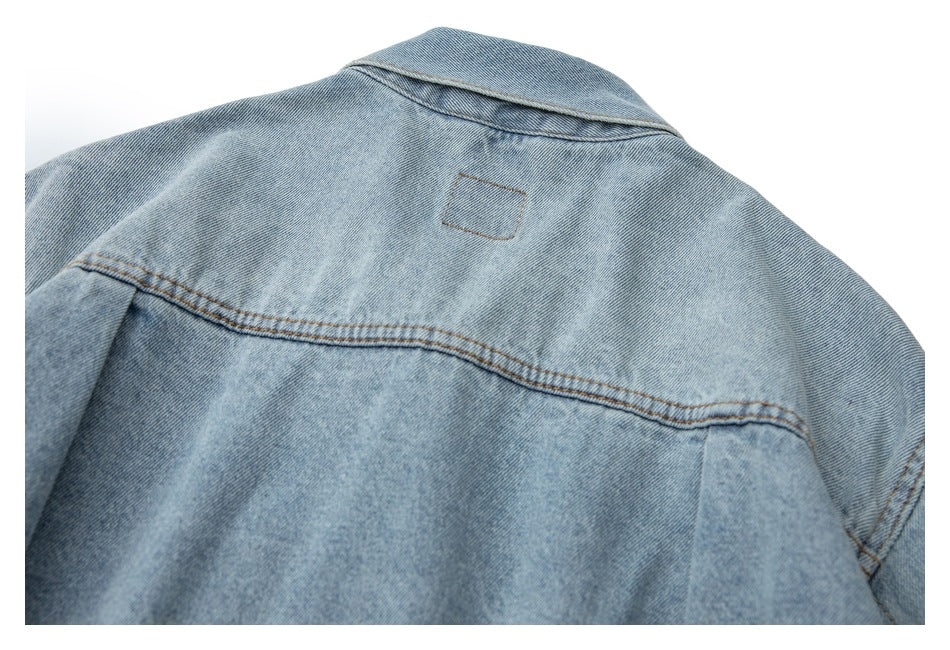 Upper back of a light blue denim jacket, showing the collar, yoke seam, and a small stitched outline.