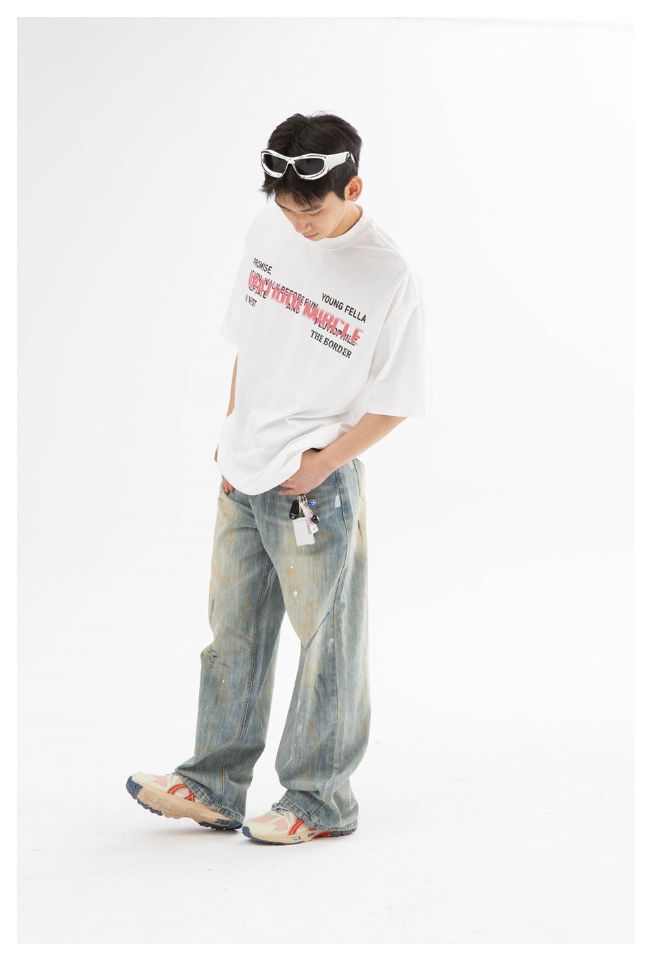 Model wearing a white graphic T-shirt and loose faded jeans, posing with one foot extended.