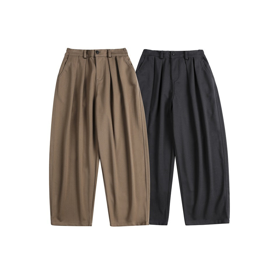 Two pairs of loose pleated trousers shown flat, one brown and one charcoal.