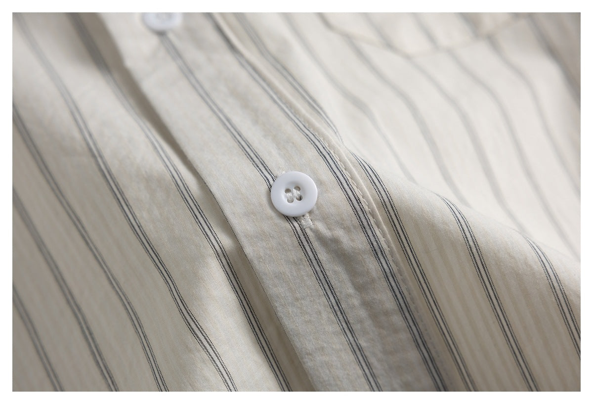 Close-up of the white button and placket on an ivory shirt with fine dark stripes.