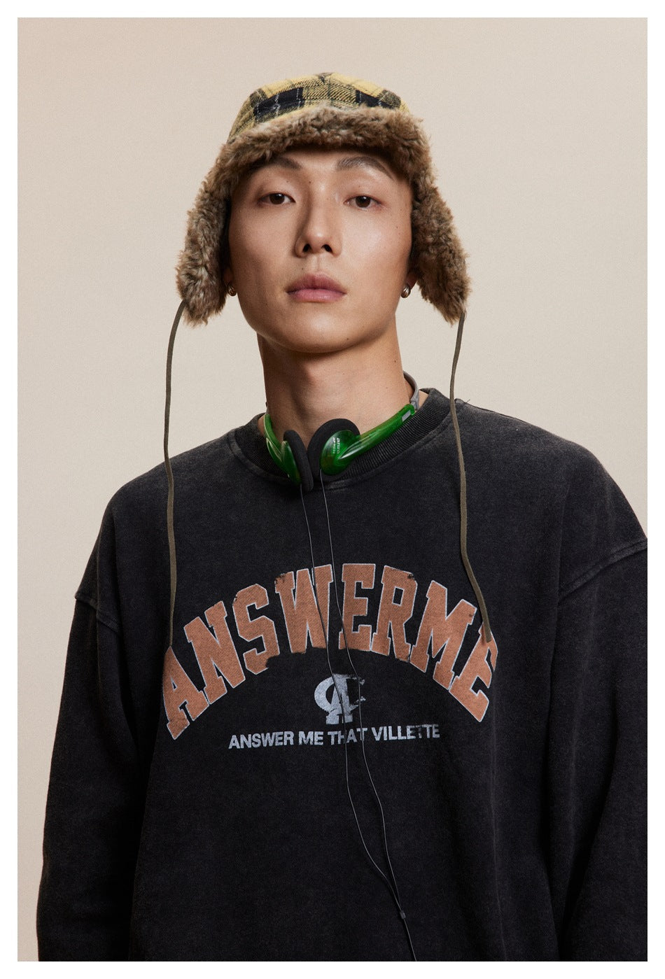 Front close-up of a model wearing a charcoal sweatshirt with large arched lettering and a smaller chest graphic.