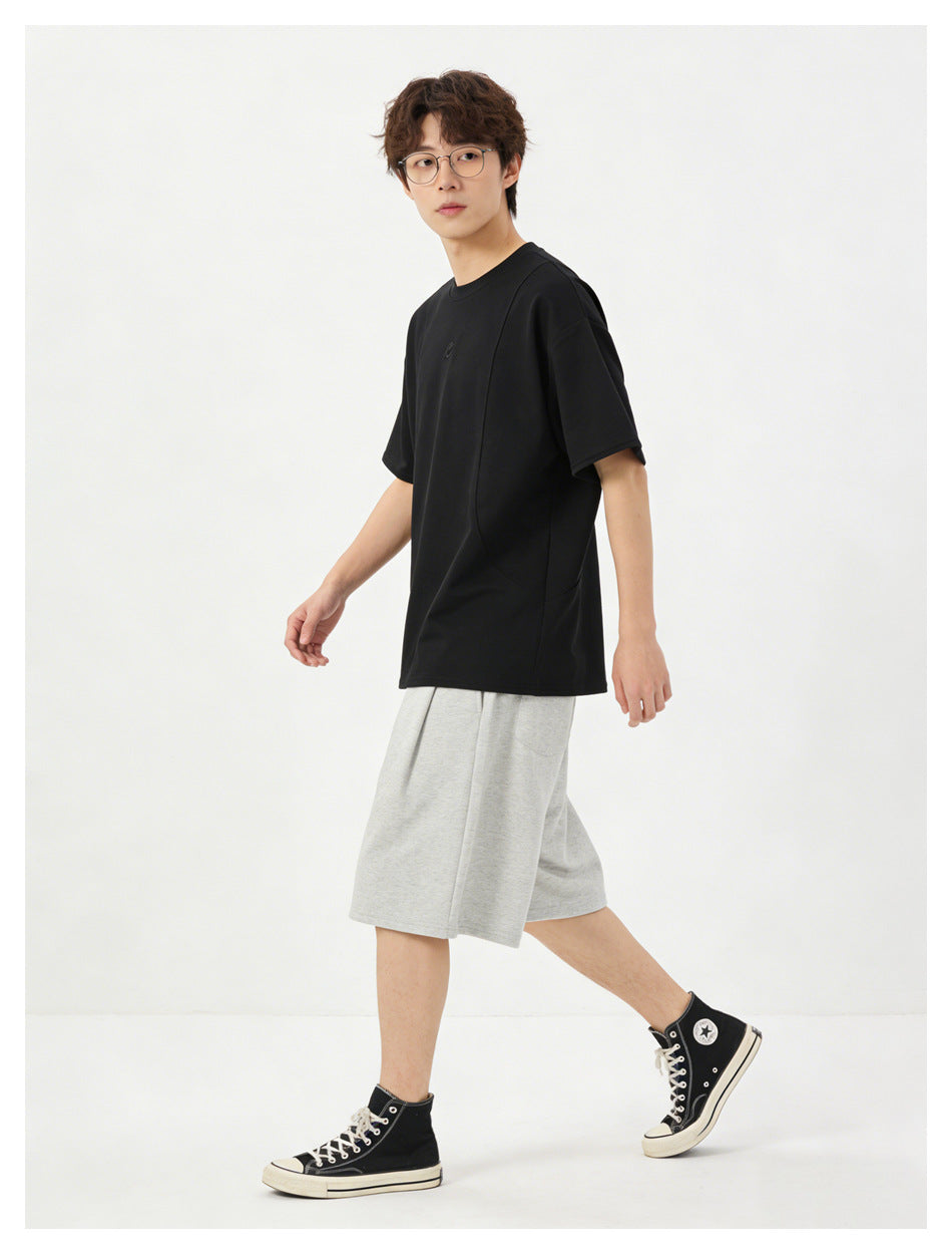 Model wearing a loose black short-sleeve T-shirt and light gray knee-length shorts, shown in a walking pose.