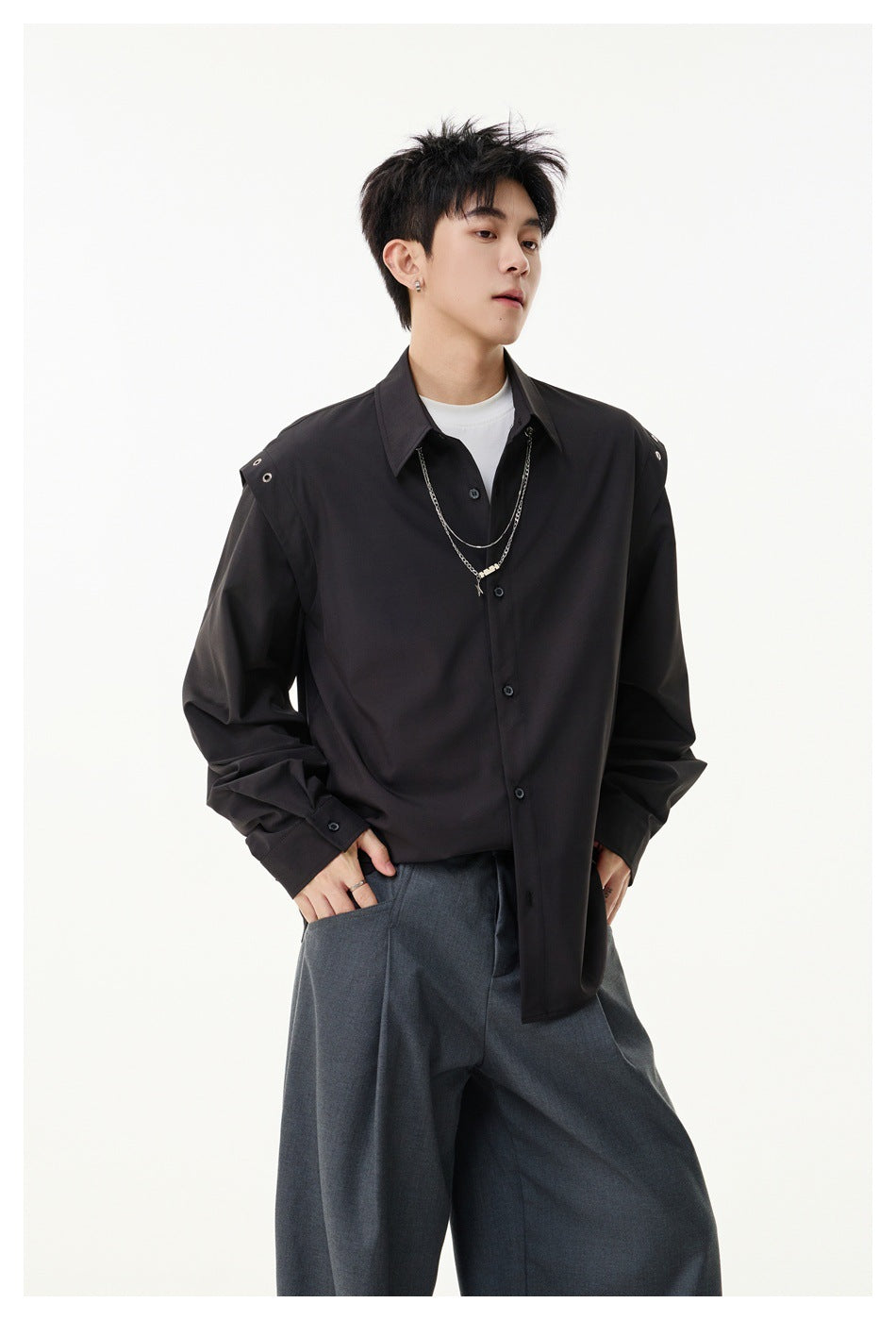 Model wearing black button-up shirt with eyelet shoulder straps and layered chain over a white tee and gray trousers