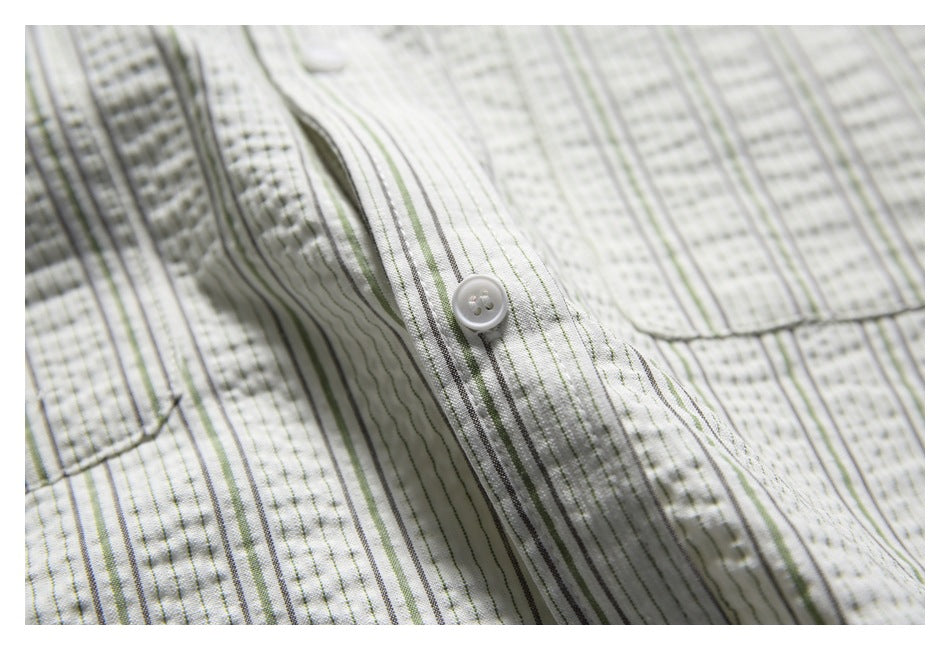 Close-up of a white button and stitched placket on an off-white shirt with fine gray and muted green stripes.