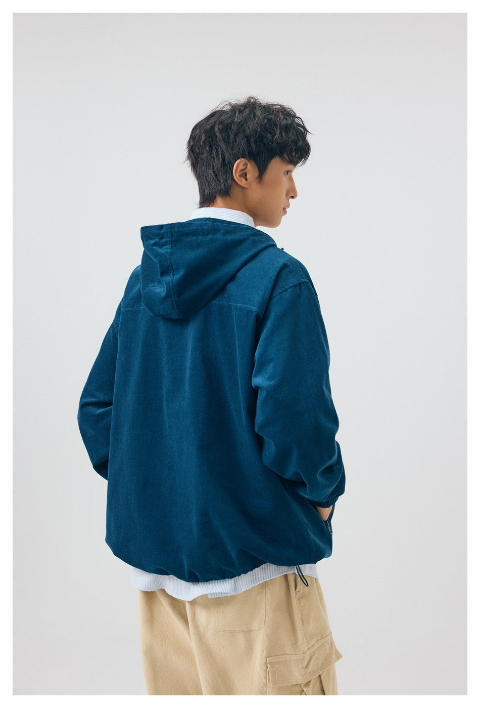 Back view of a model wearing a deep teal hooded pullover with beige cargo pants.