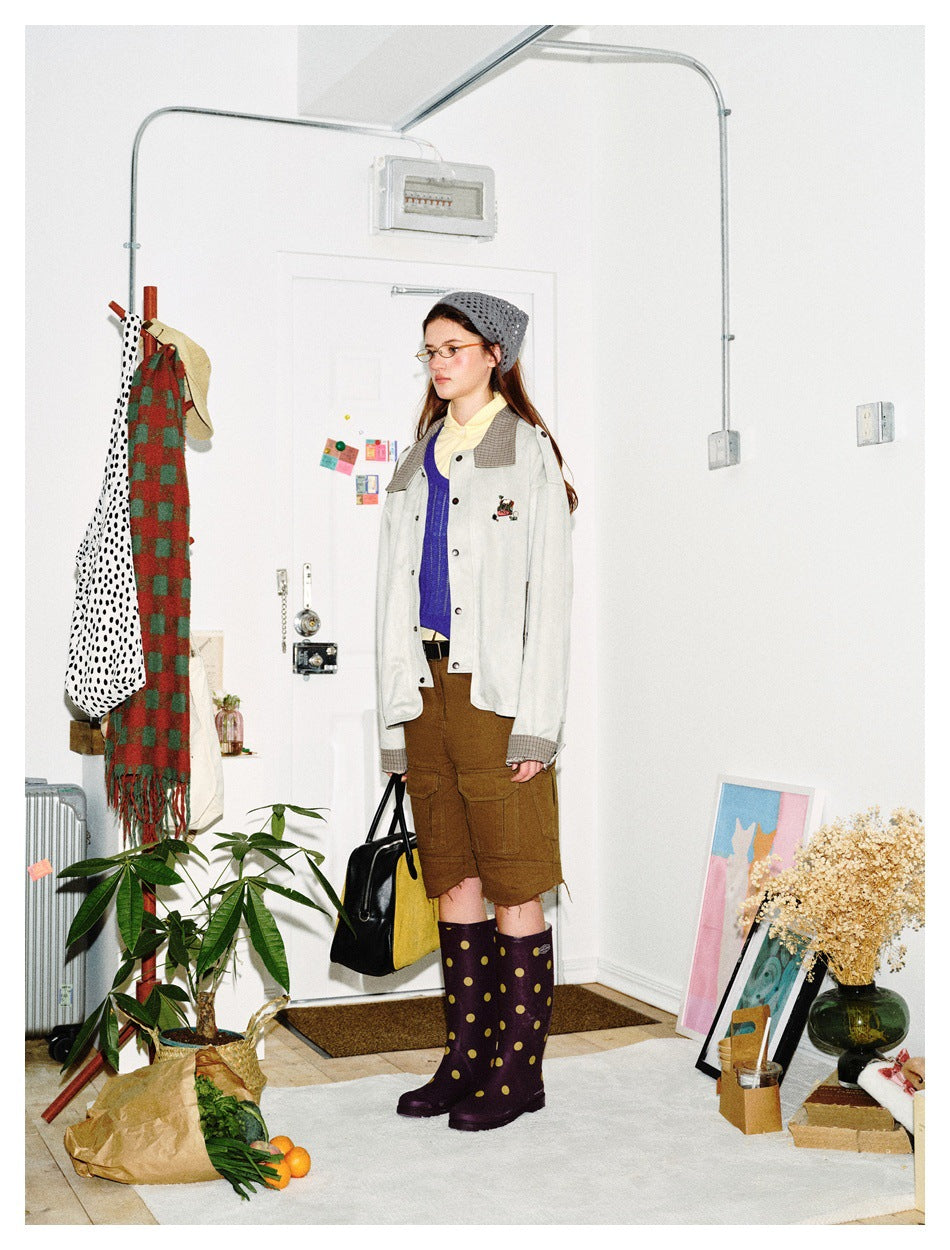 Three-quarter view of a model wearing an ivory jacket with plaid collar and cuffs, brown shorts, and polka-dot boots.