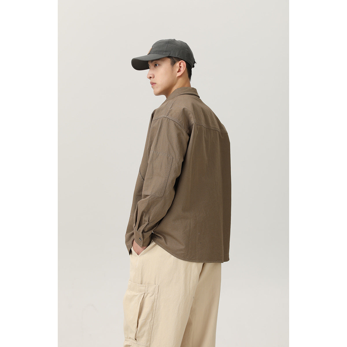 Side and back view of a model wearing a brown overshirt with a back yoke and cream cargo pants.