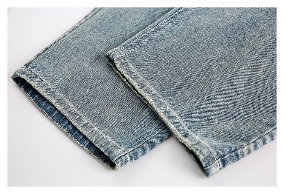 Close-up of the straight hems on light blue faded jeans, laid flat.