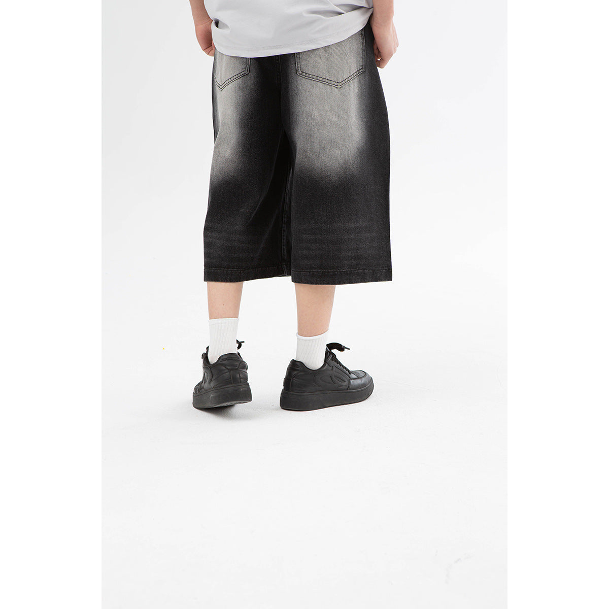 Close rear view of washed black wide-leg shorts, showing two back pockets and faded gray areas.