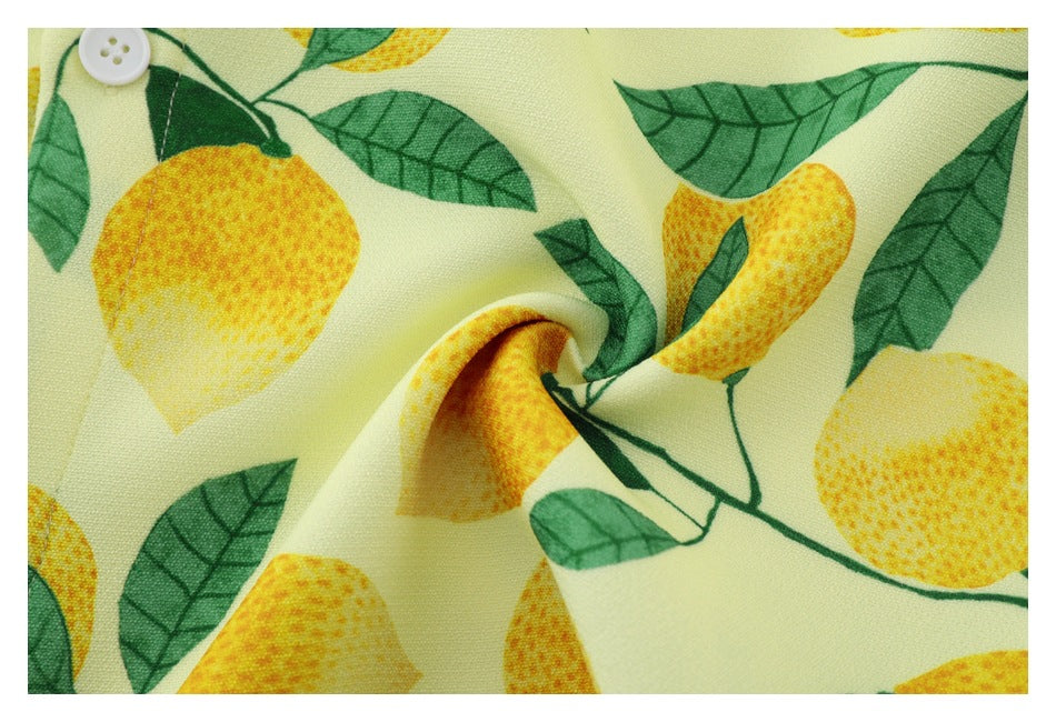 Close-up of the pale yellow shirt’s lemon-and-leaf print, showing a white button and a fold in the fabric.